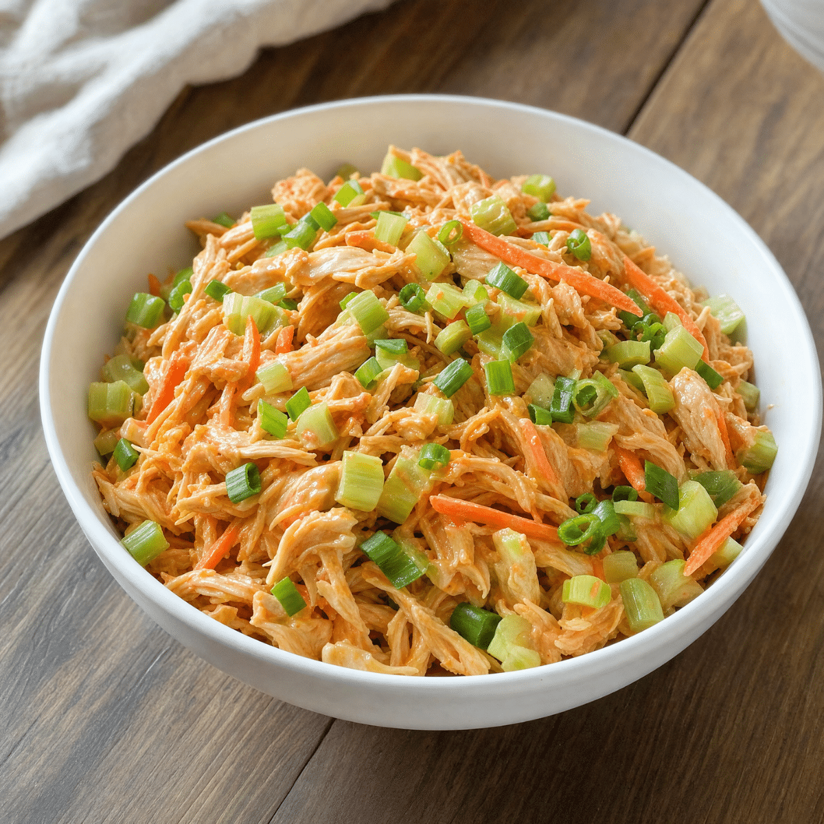 Healthy Buffalo Chicken Salad with shredded chicken, Greek yogurt buffalo dressing, celery, carrots, and green onions served in a white bowl.